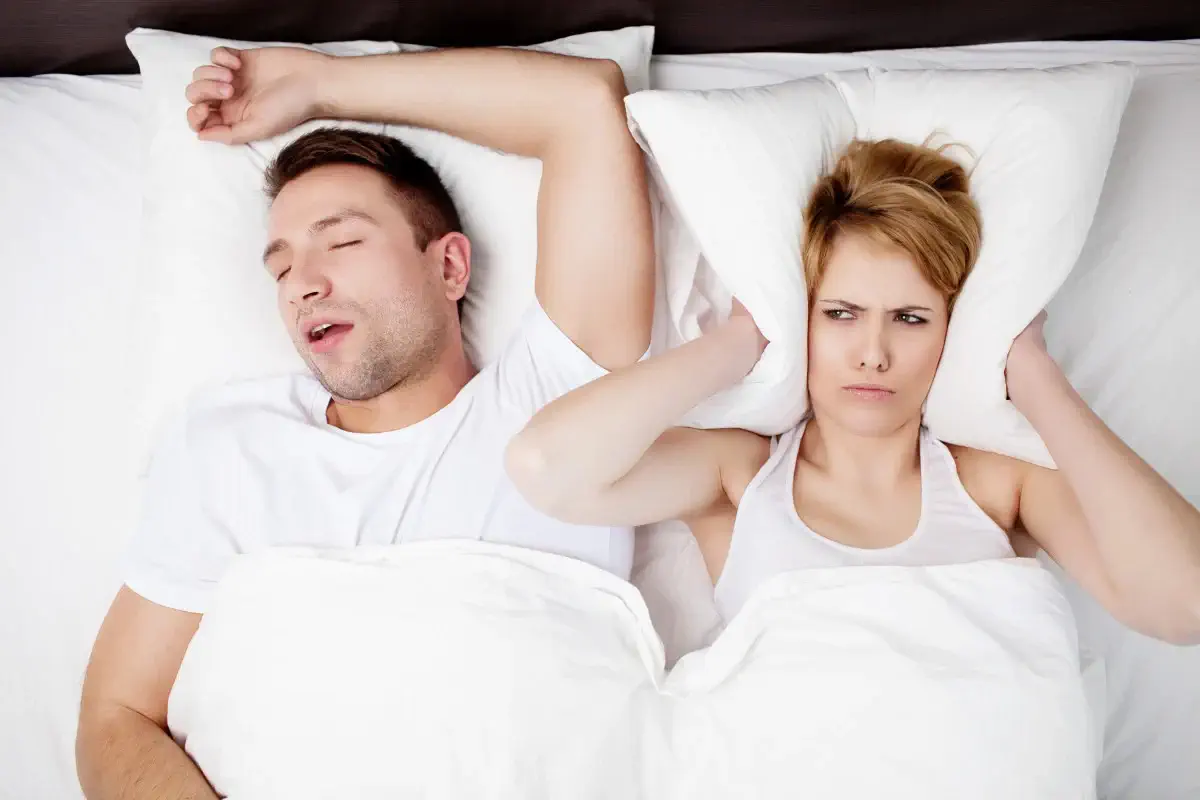 wife covering her ears as husband is snoring beside her